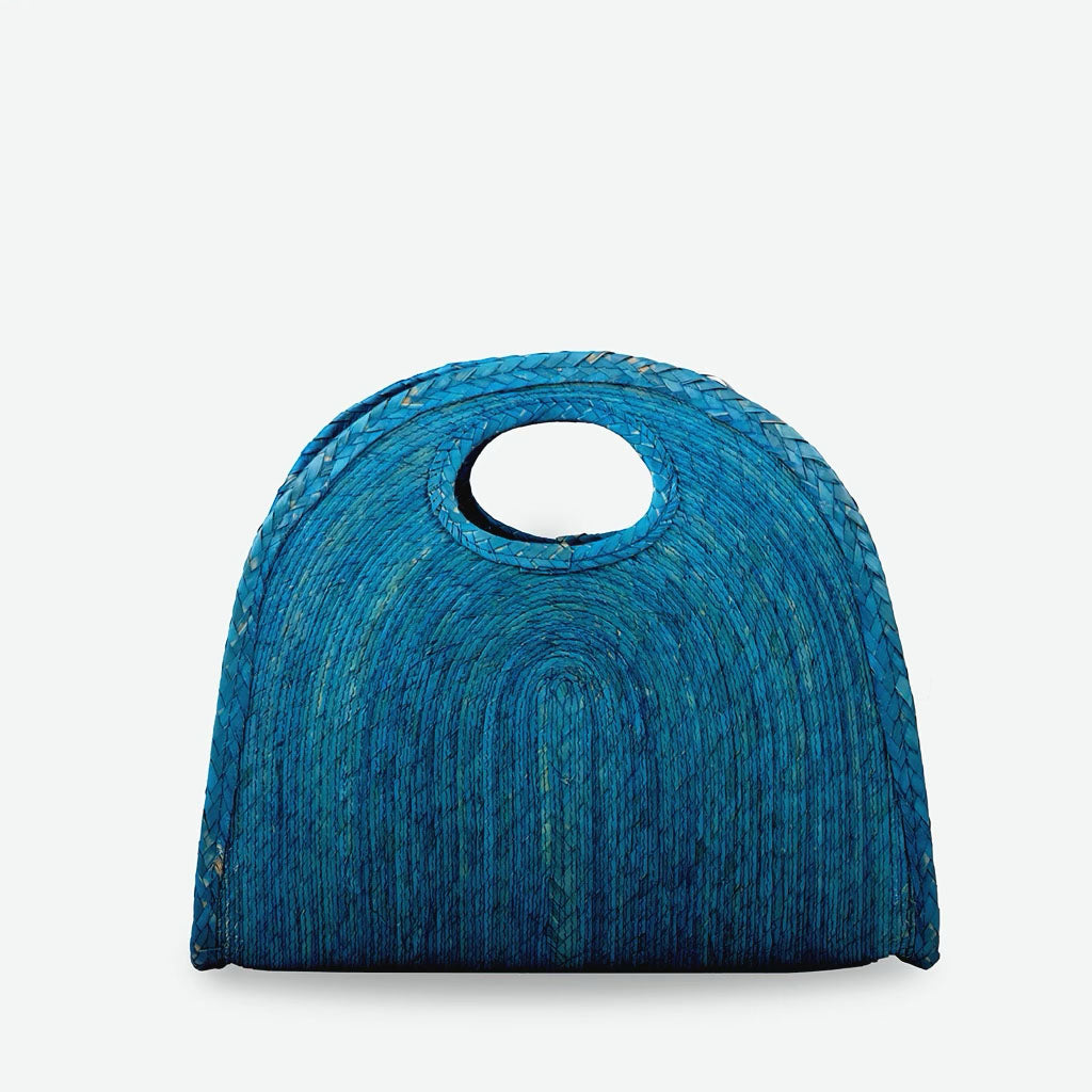 Teal handheld crescent straw tote bag, woven from palm and dyed with organic colors. Summer-ready design by Per Lei New York.