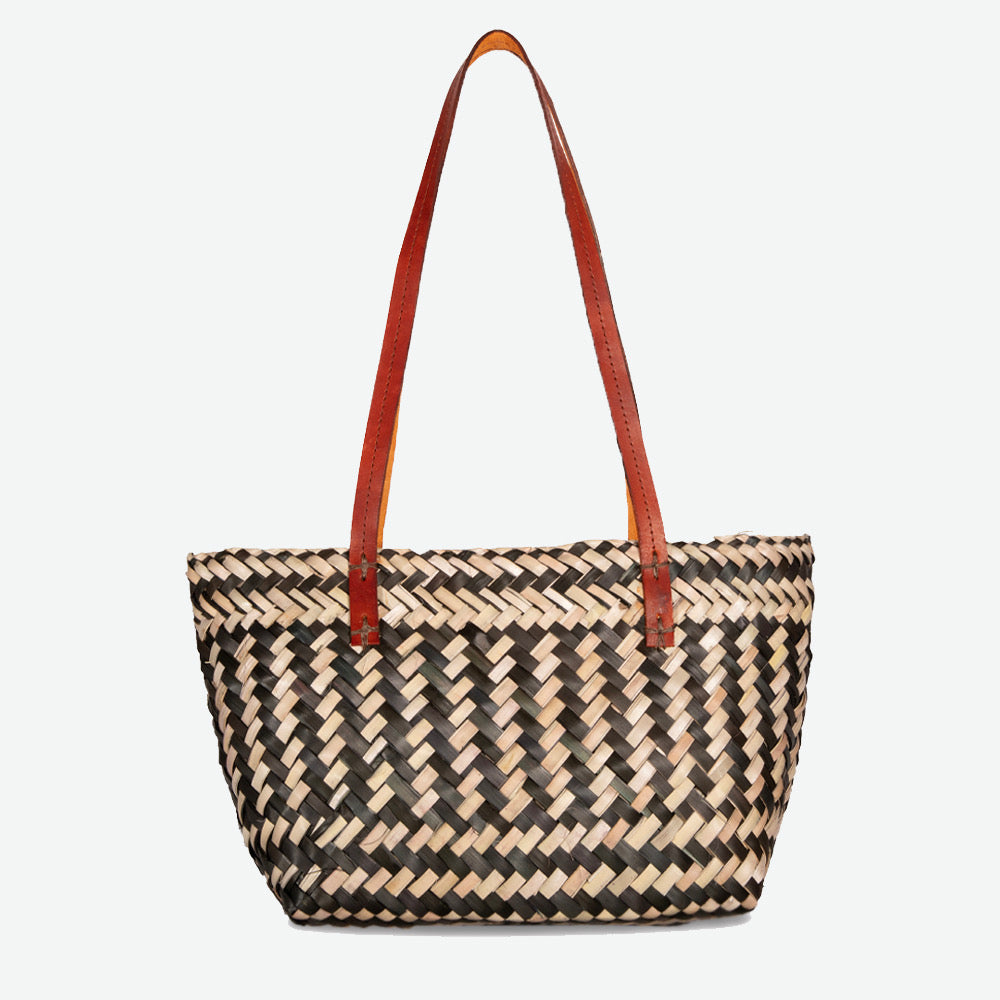 Black and white woven straw handbag with brown leather handle on a white background