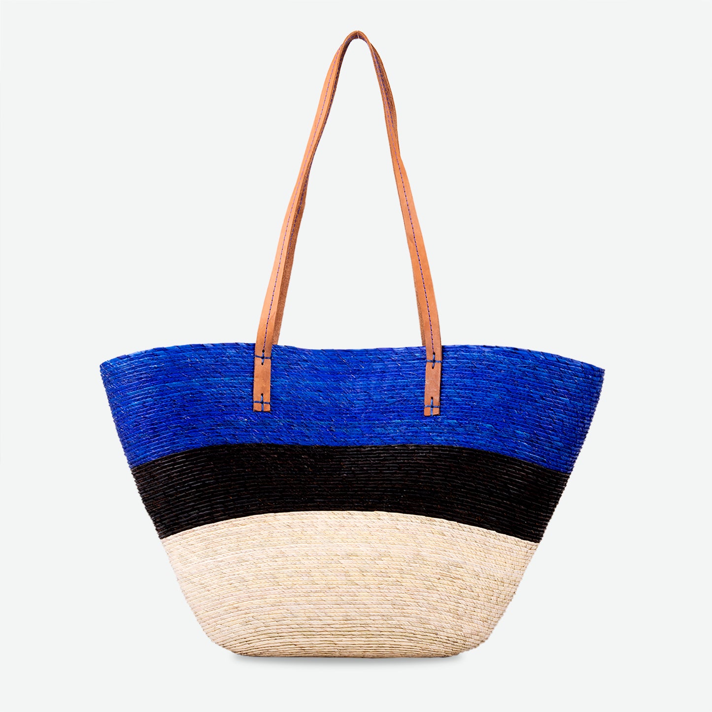 Large straw market tote in blue, black, and natural with brown leather straps, handwoven and standing upright.